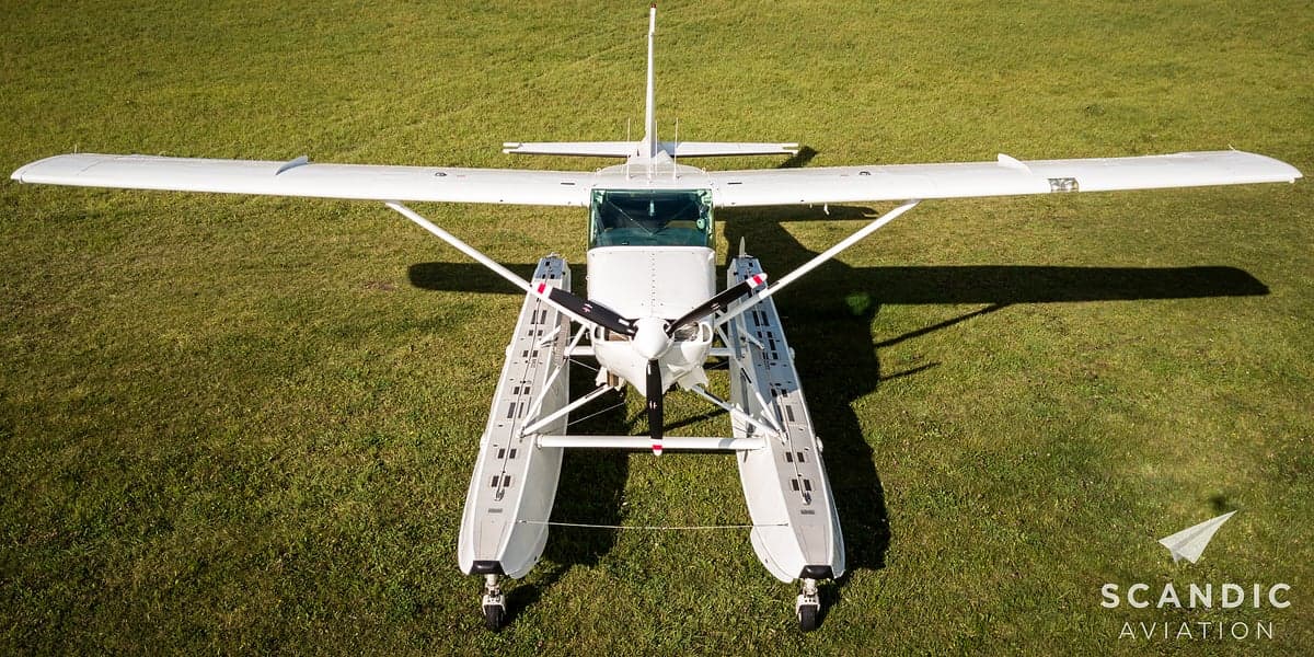 Overhead view of a white floatplane on a grassy field.