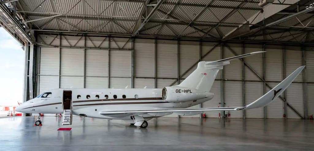 A white Embraer Praetor 600 business jet with brown stripes and its door open is parked inside a hangar.