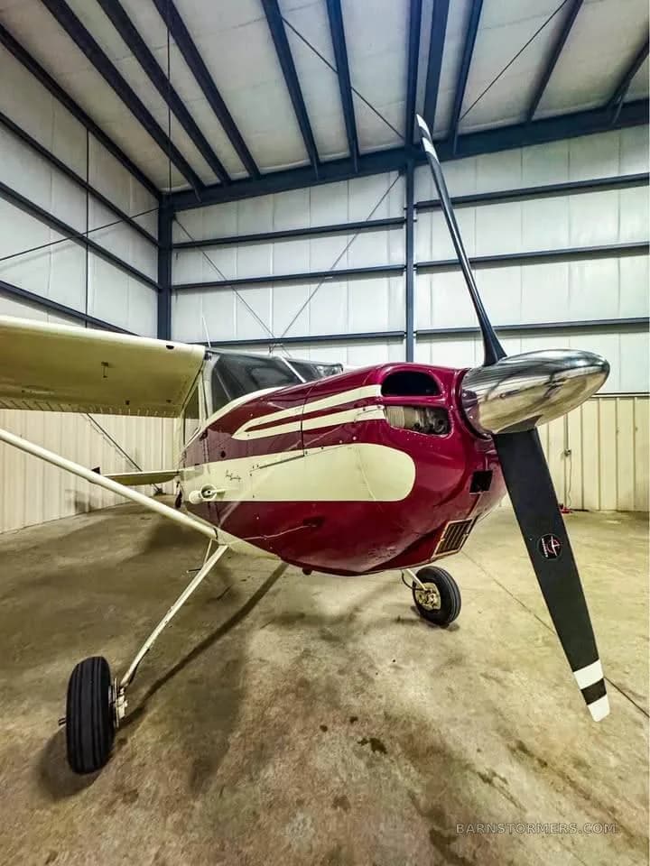 A front-quarter view of a red and white single-engine propeller aircraft in a hangar.