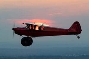 A red Cubcrafters aircraft is flying at sunset.