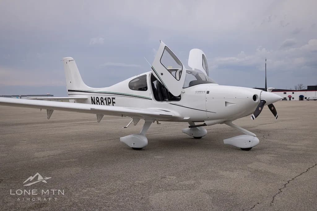 A front-side view of a white Cirrus SR22 aircraft with N881PF registration and open doors, parked on an asphalt ramp.