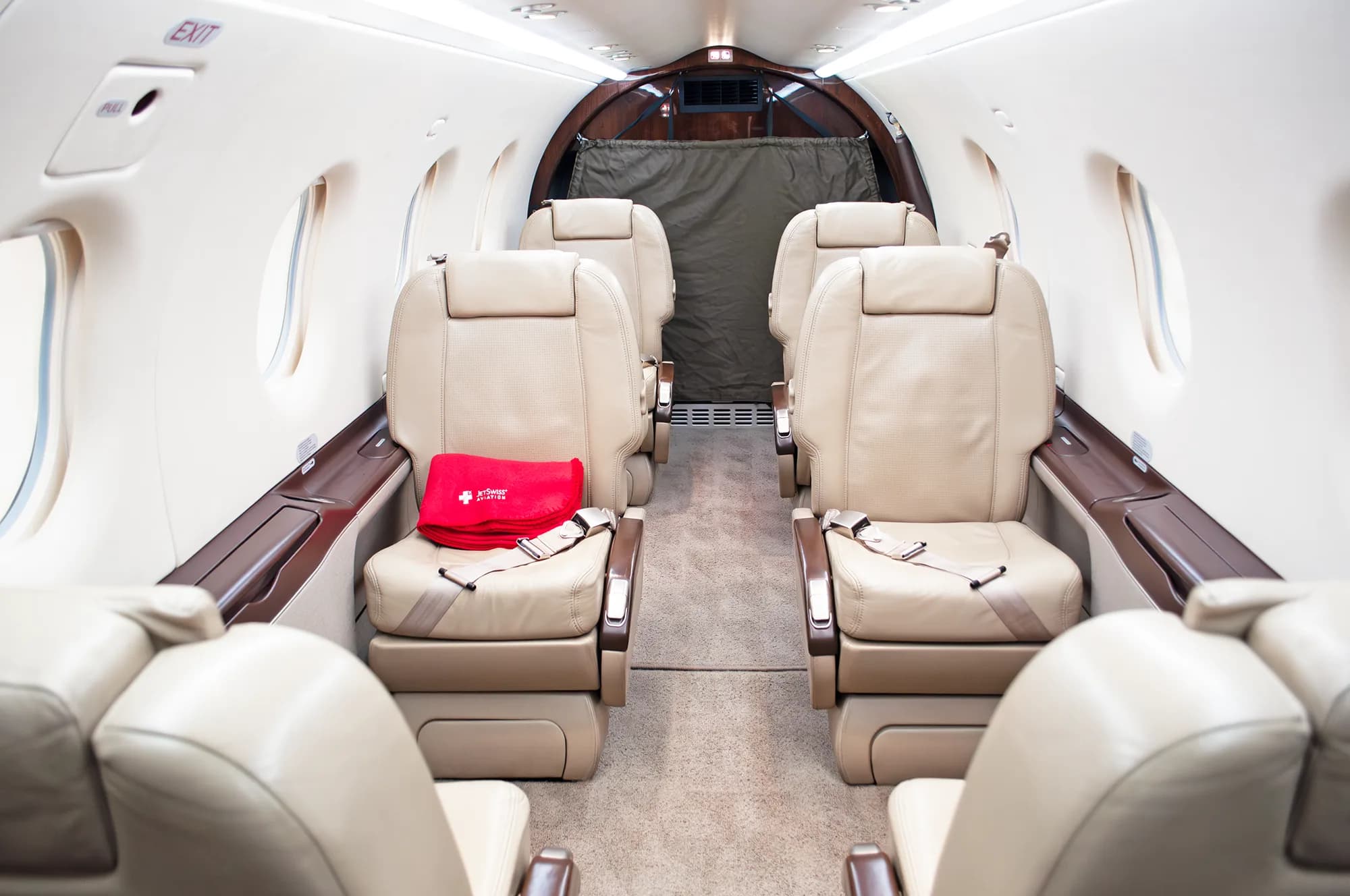 The interior cabin of a Pilatus PC-12 NG aircraft, showing beige leather seats arranged in a club configuration.