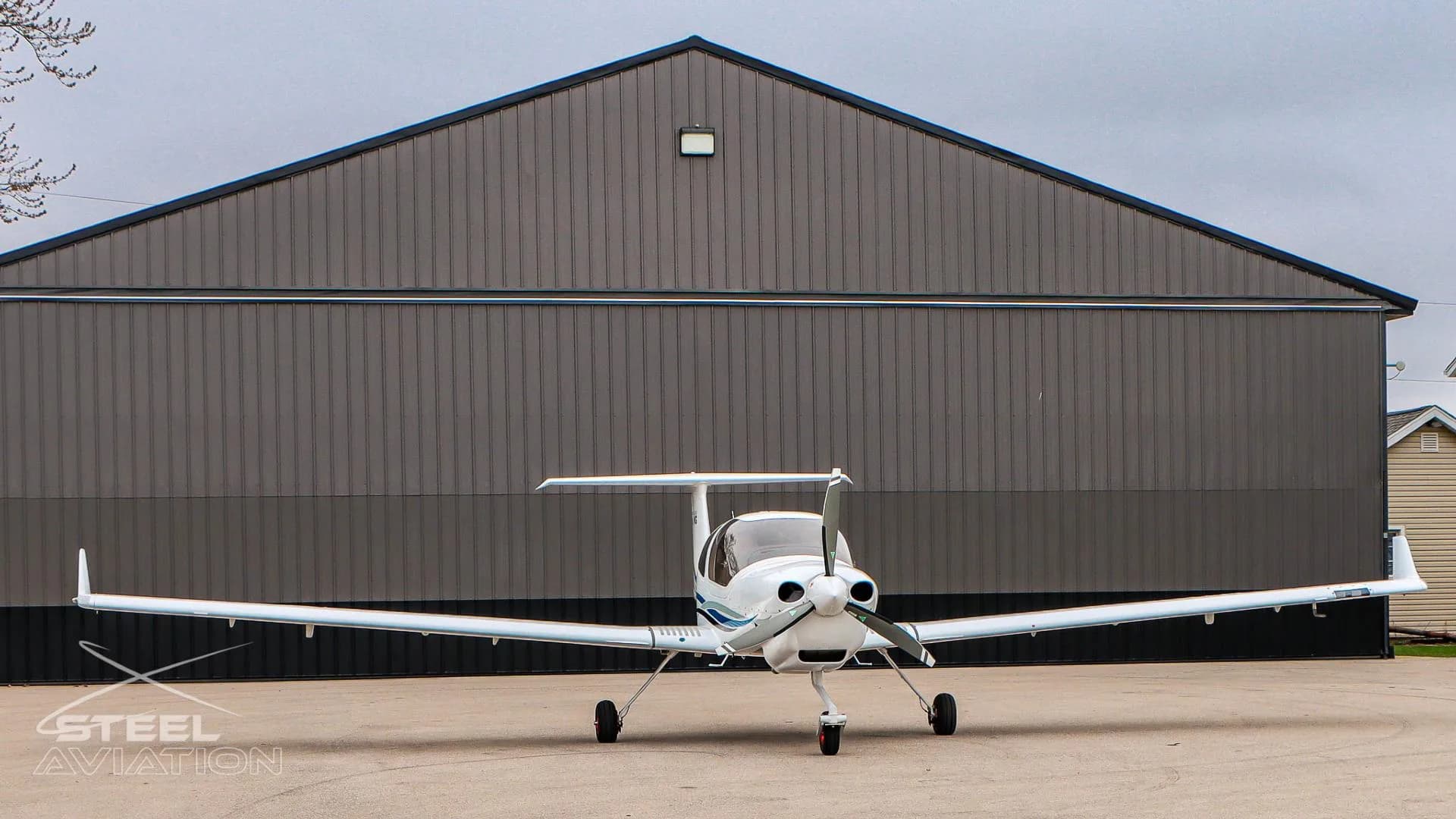 Front view of a white Diamond DA40 NG aircraft with blue and grey stripes parked in front of a hangar.