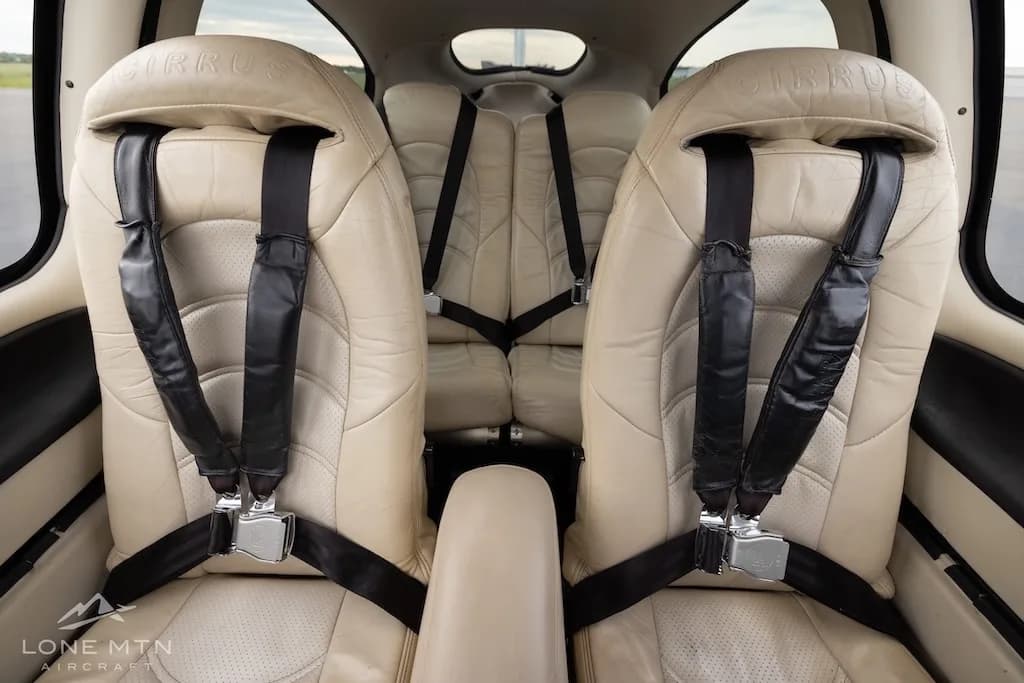 View of the two rear beige leather seats with black harnesses in the aircraft cabin.
