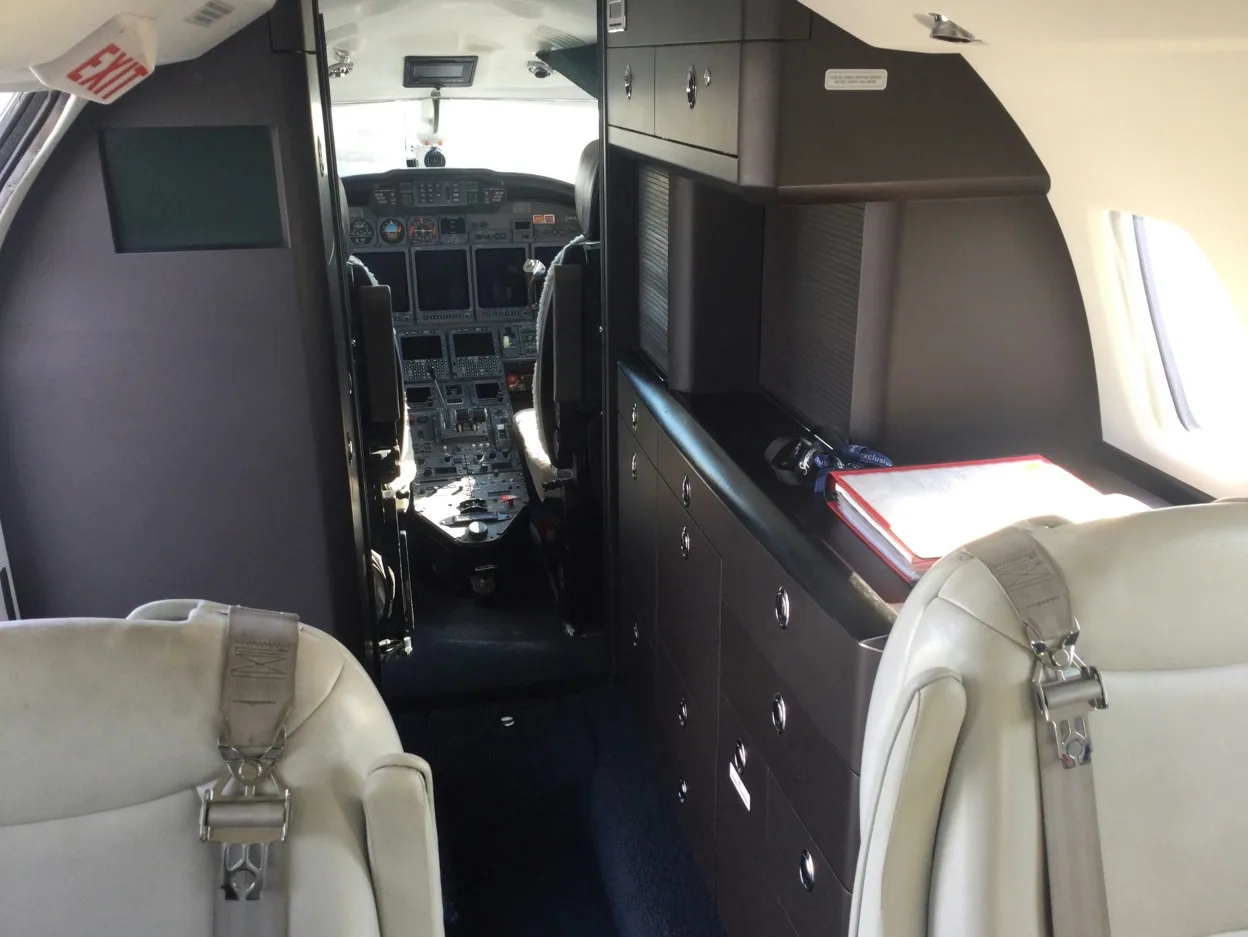 Aircraft cabin with light gray leather seats and a view towards the cockpit.