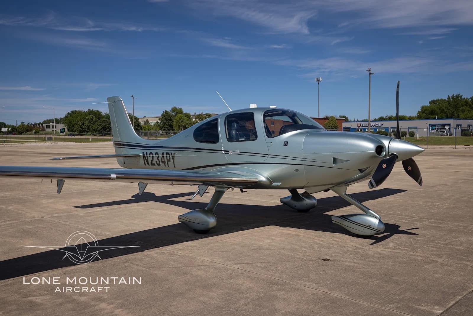 A silver Cirrus SR22 aircraft with black stripes (N234PY) parked on a tarmac under a blue sky.
