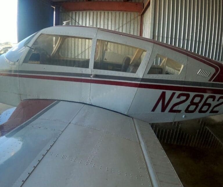 Close-up of the side of a white and red Piper PA-28-140 Cherokee in a hangar, registration N2862 visible.