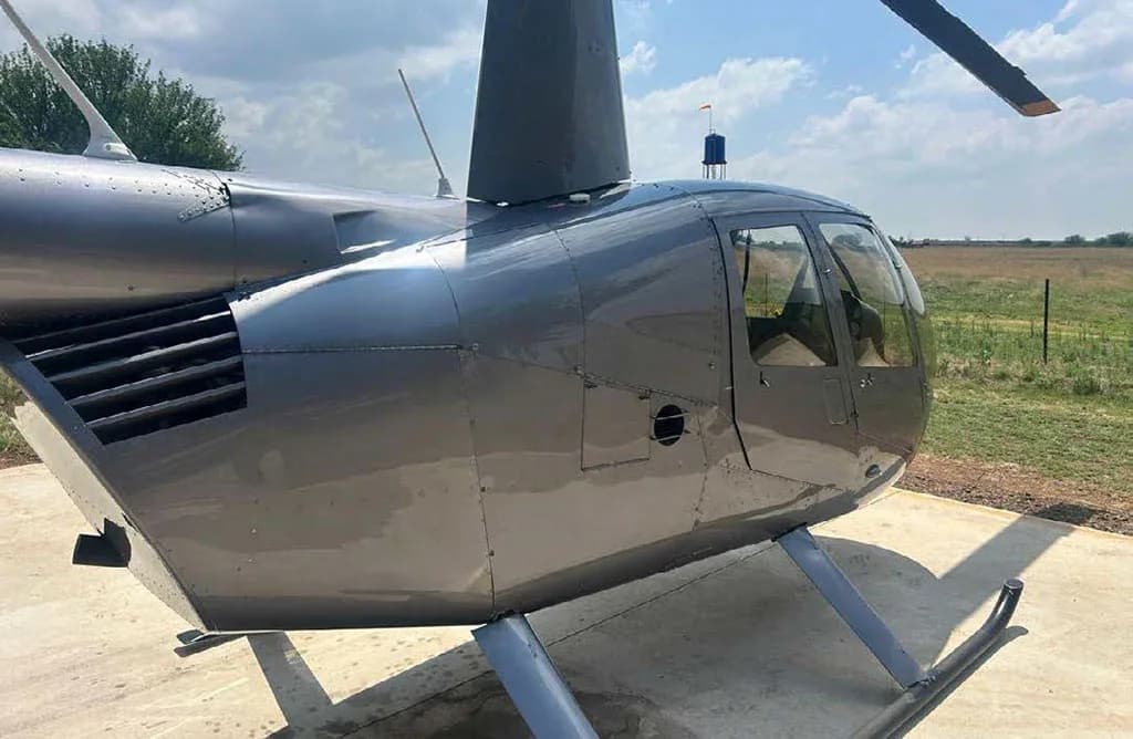 A close-up side view of the cockpit and engine vents of a silver Robinson R44 helicopter.