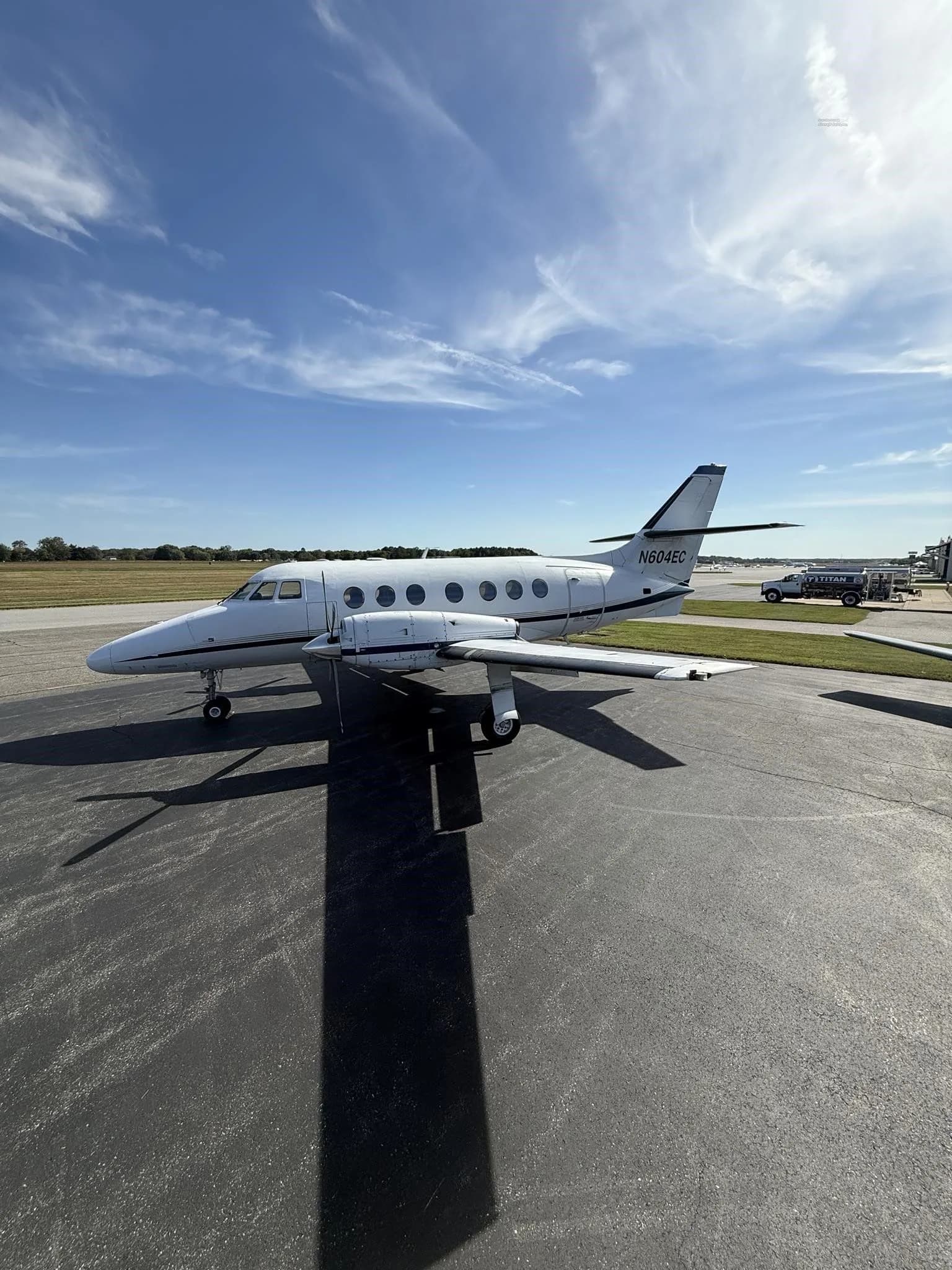 A side view of a white Jetstream 31 aircraft with blue accents, tail number N604EC, parked on an asphalt tarmac with a service vehicle in the background.