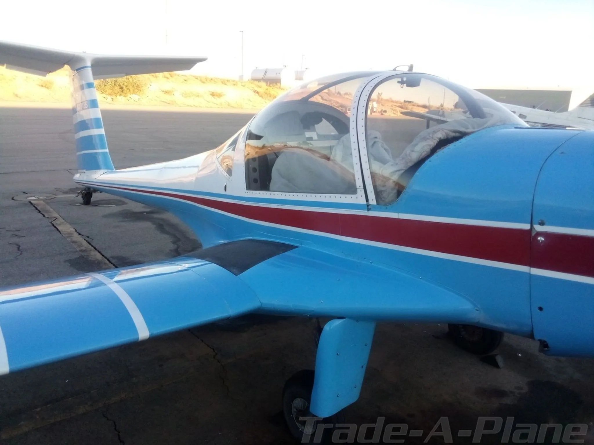 A close-up, rear-quarter view of a blue and white aircraft with a red stripe, parked on an tarmac.