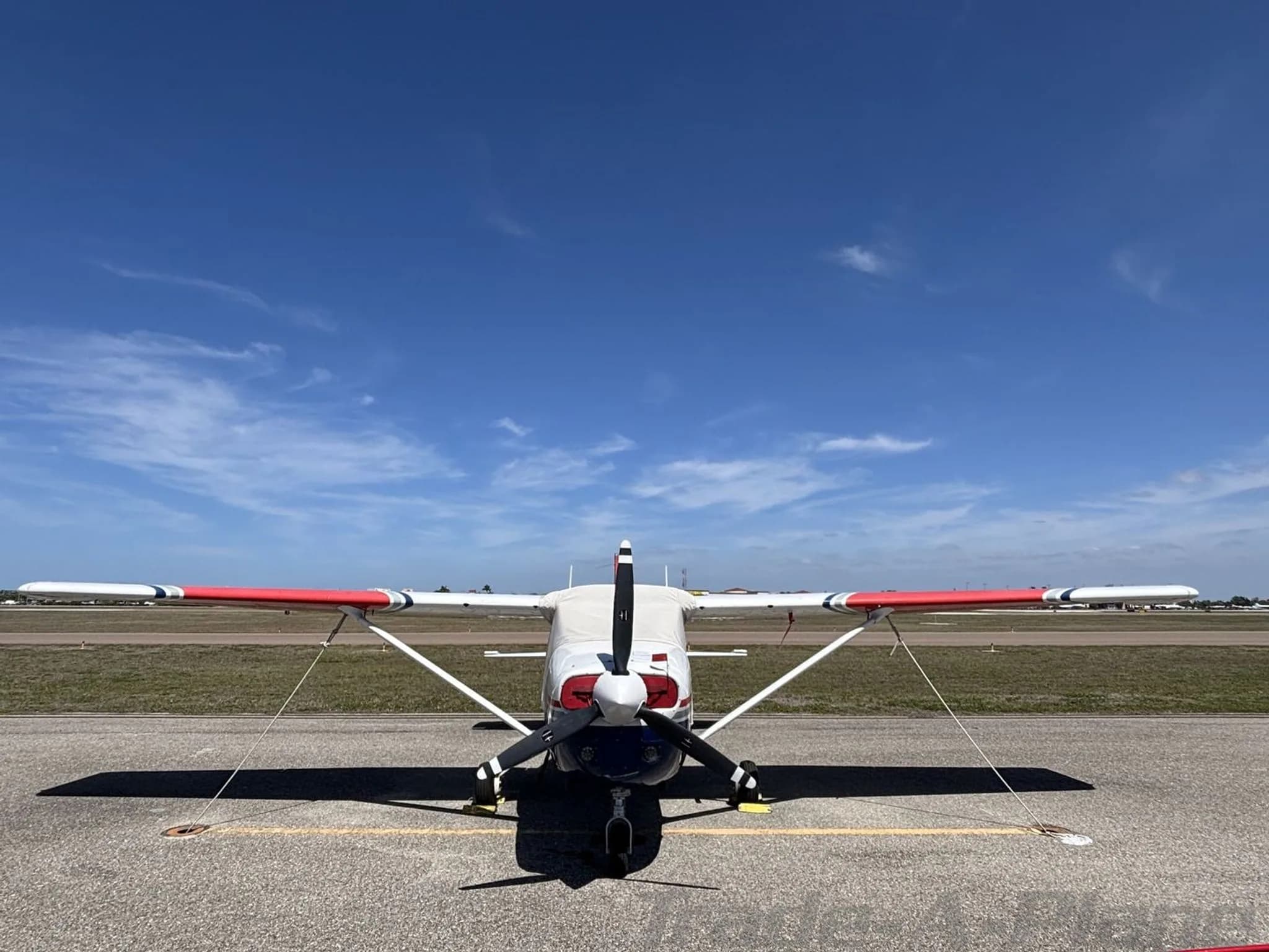 Front view of a white, blue, and red Cessna N7360C with its propeller, parked on an airfield.