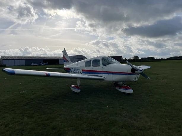 A Piper PA-28-181 Archer II aircraft, registration N735FL, is parked on a grassy field.