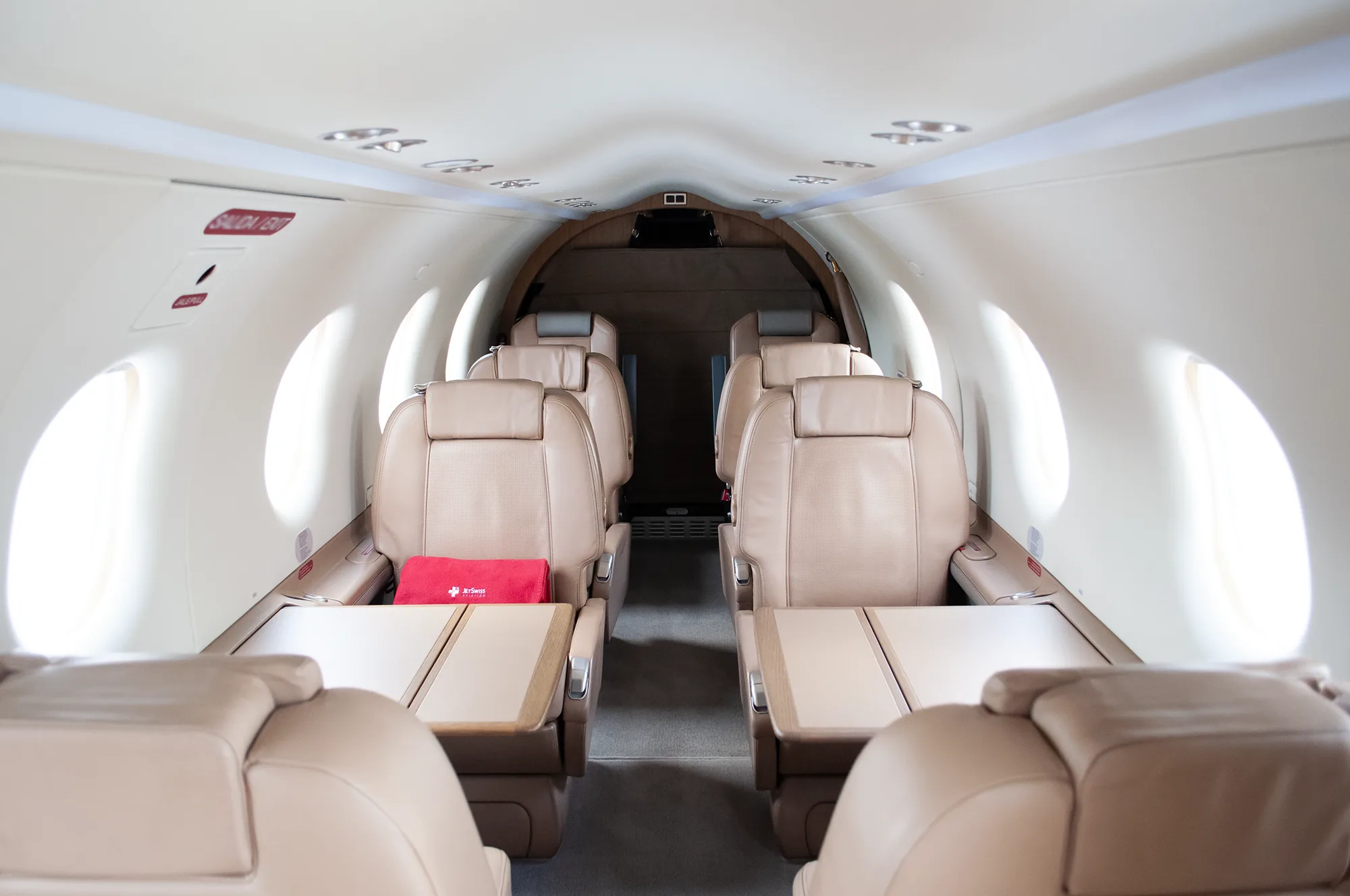 View down the cabin aisle of a Pilatus PC-12, showing tan leather seats and fold-out tables.