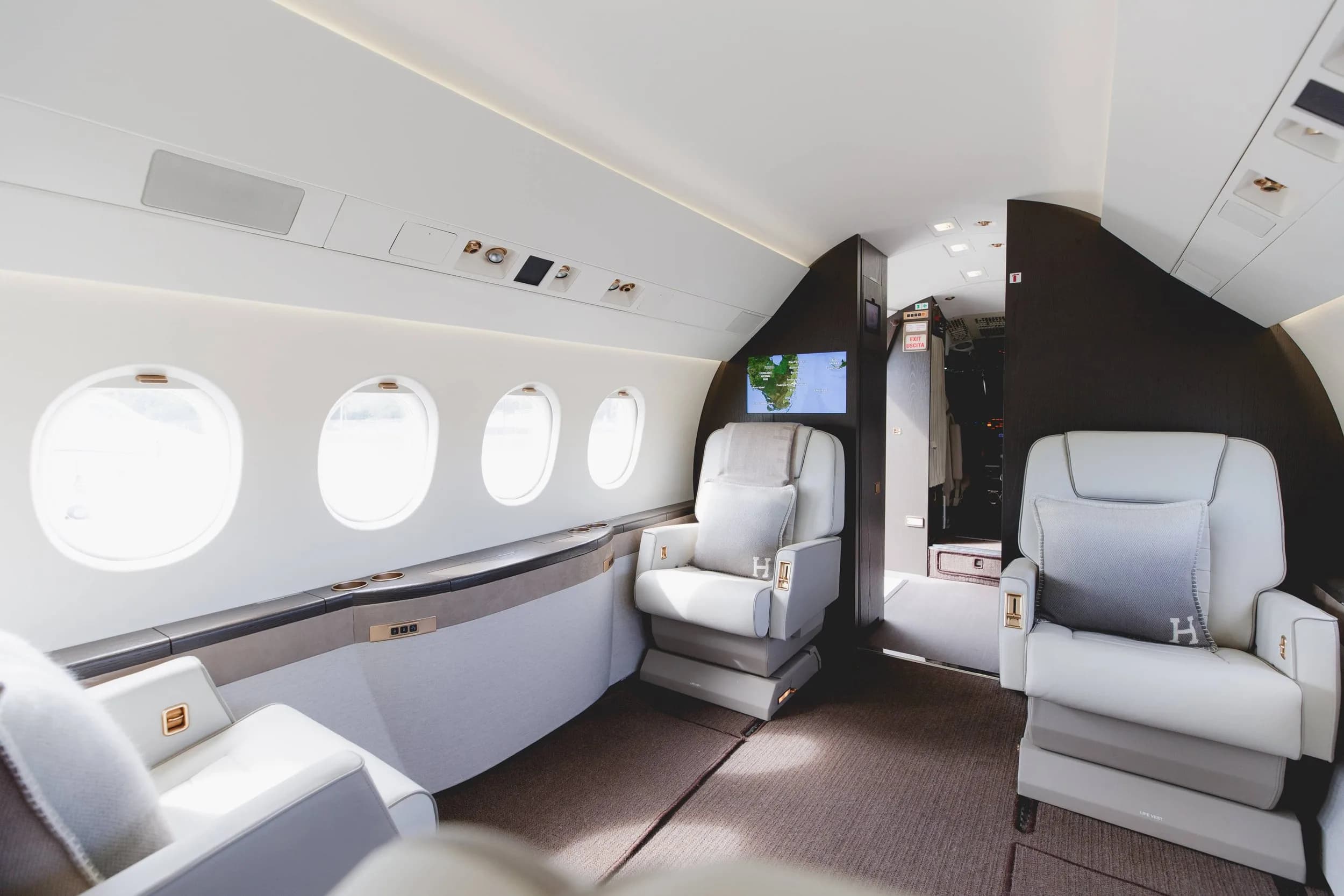 An angled view of the aircraft cabin showing white leather seats, windows, and a screen displaying a map.