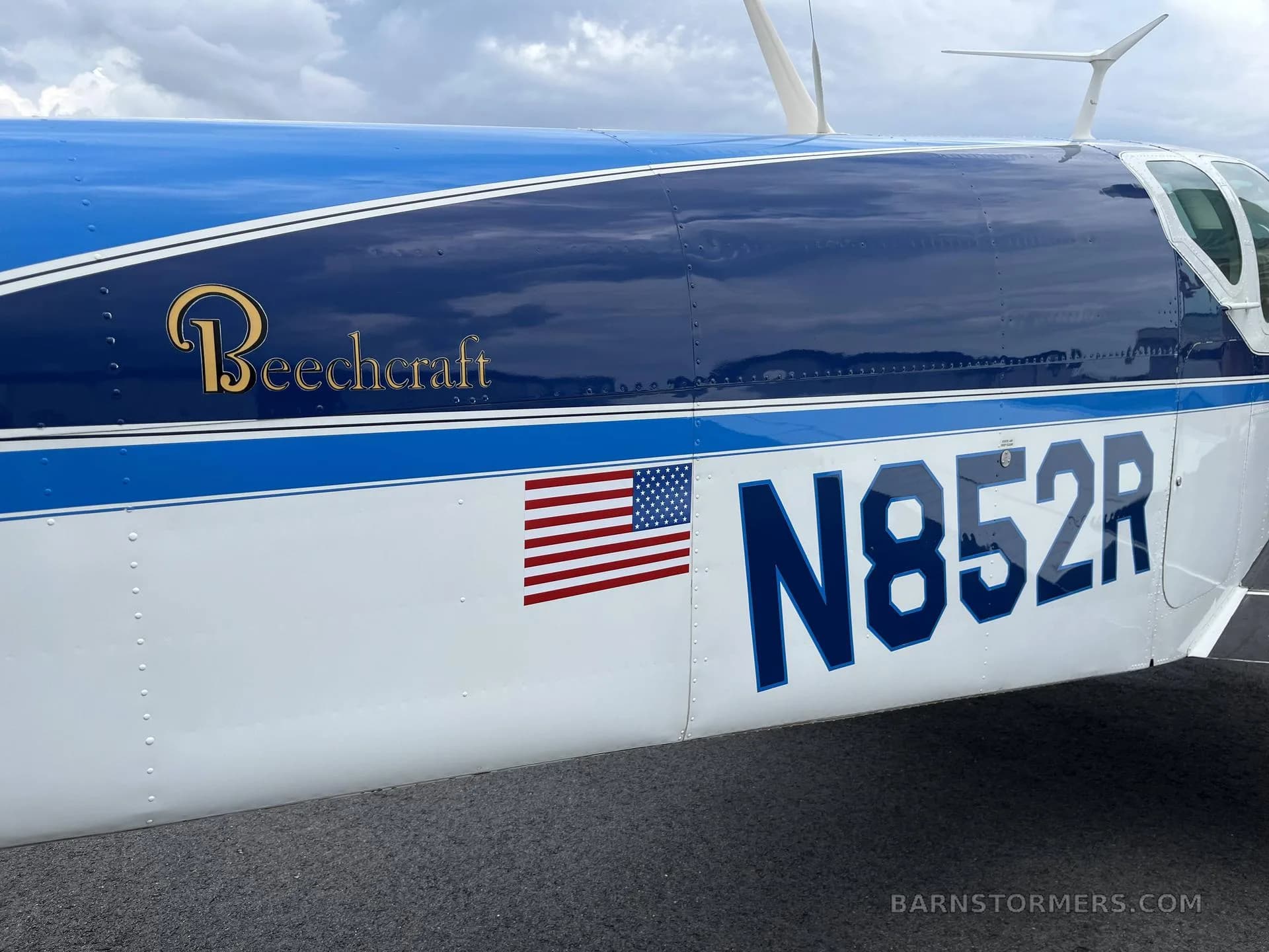 A close-up of the blue and white fuselage of a Beechcraft Bonanza N852R, showing the registration and an American flag decal.