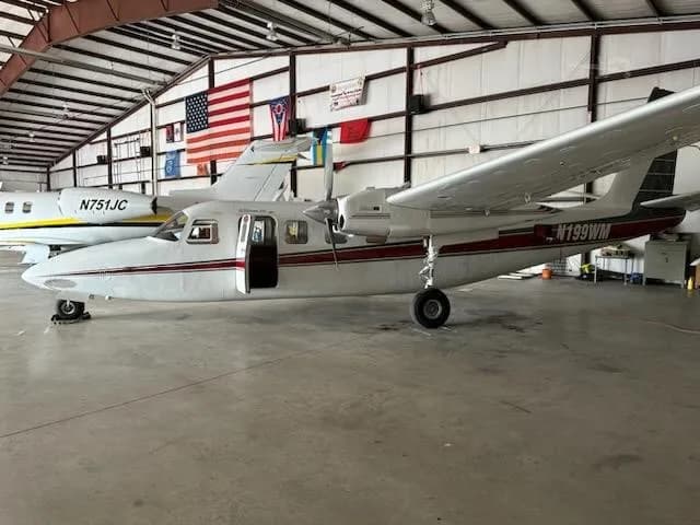 A white and red Aero Commander 680FL twin-engine aircraft, registration N199WM, parked in a hangar with its door open.