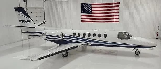 A white business jet with blue stripes, tail number N804RD, parked in a hangar with an American flag.