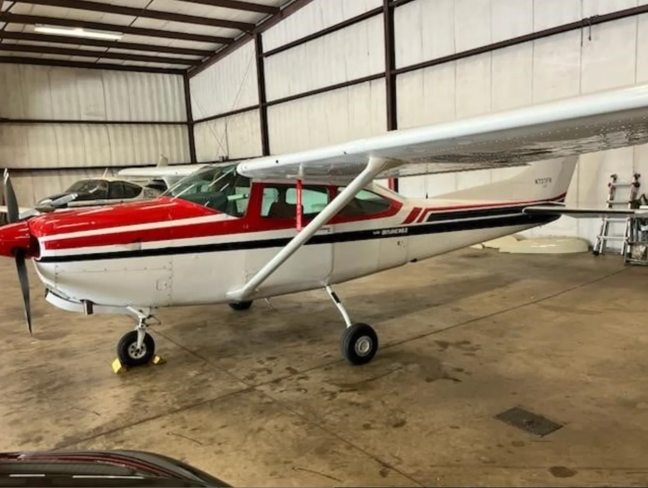 A red and white Cessna 182 Skylane (N737FR) parked inside a hangar, viewed from the side.