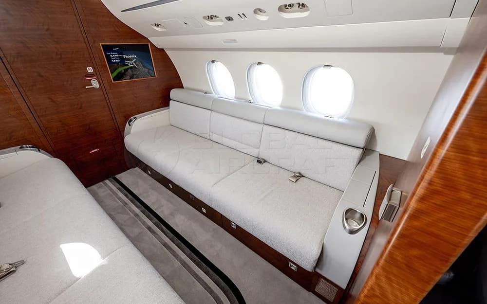 A comfortable gray sofa seating area inside a private jet cabin with wooden paneling and windows.