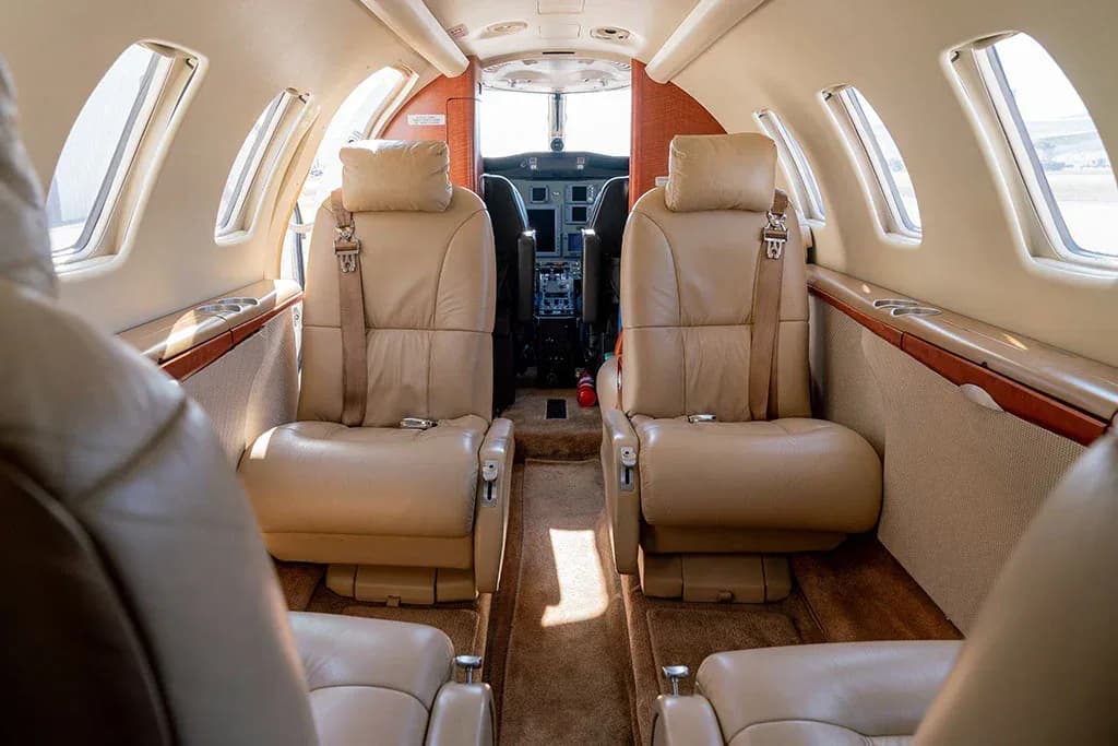 The interior cabin of a private jet, showing beige leather seats and a view into the cockpit.
