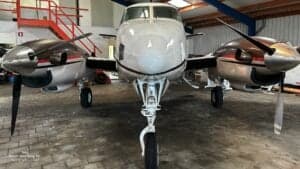 A Beech B90 King Air aircraft is shown head-on inside a hangar.
