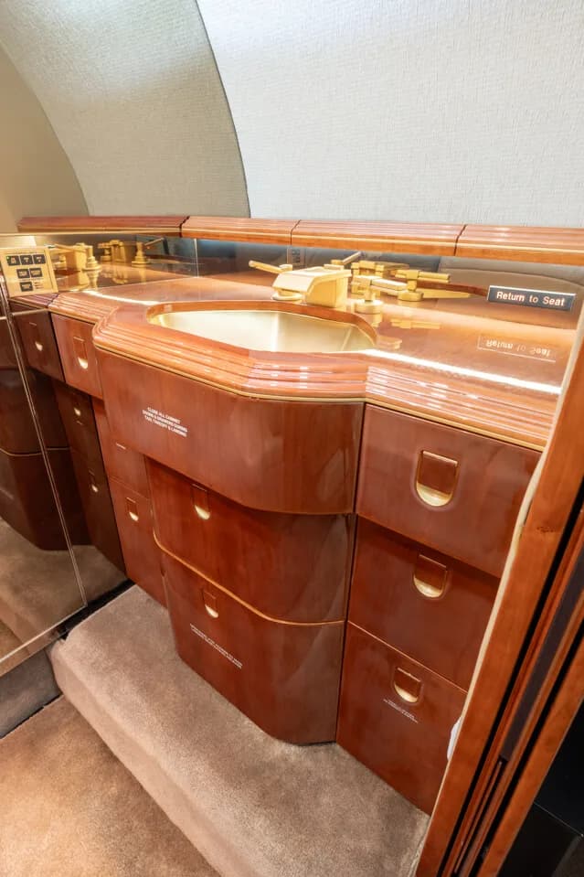 A close-up of the lavatory sink and polished wood vanity in the aircraft's interior.