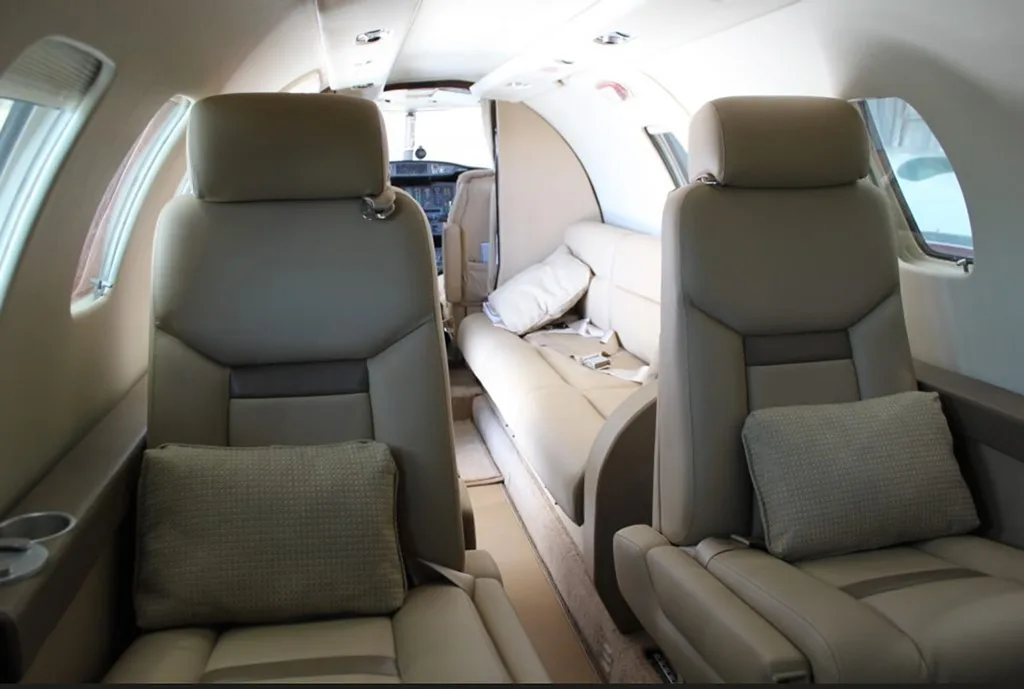A view down the aircraft cabin aisle showing beige leather seats and a side couch.