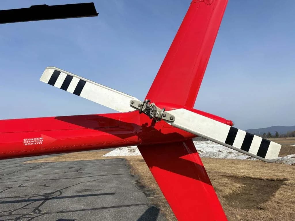 A close-up view of the red tail section and black-and-white striped tail rotor blades of a helicopter.