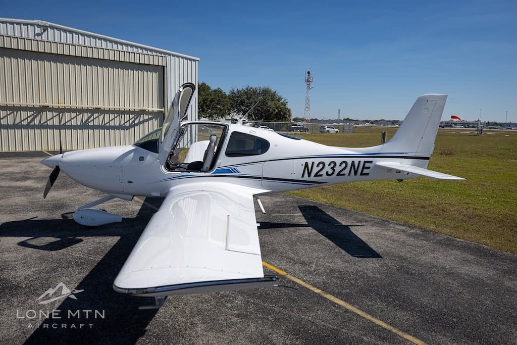 Cirrus SR22T aircraft N232NE parked near a hangar with open doors.