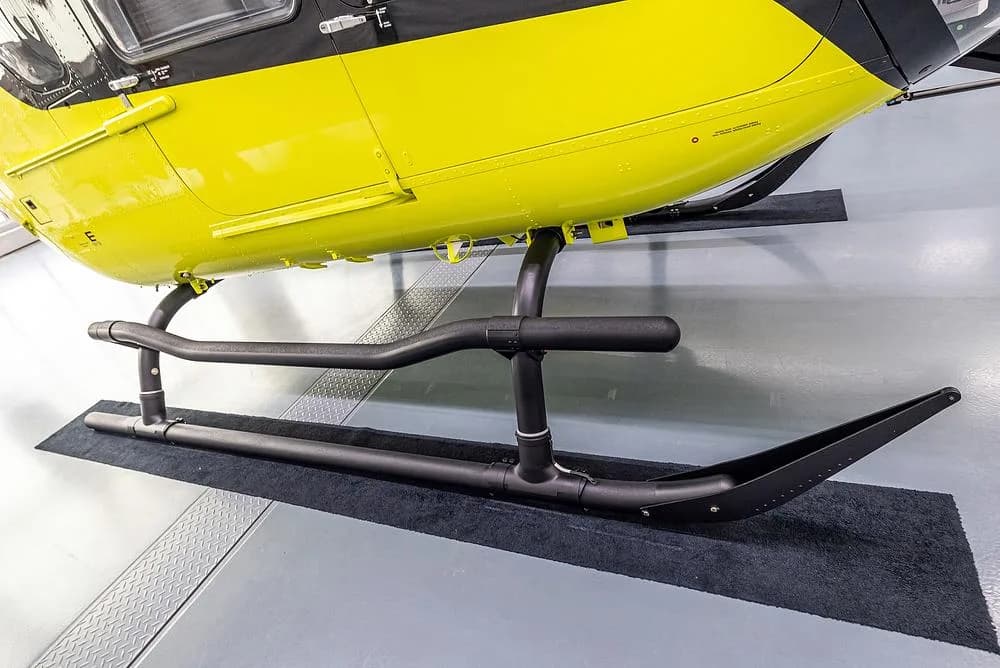 A close-up view of the black landing skids and underside of a yellow Airbus H135 helicopter.