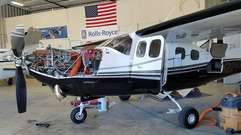 A black and white Cessna 208B Grand Caravan, registration N22VF, is in a hangar with its engine cowling open.