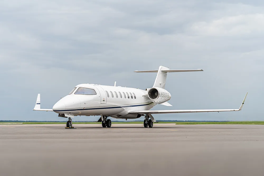 A white Cessna Citation business jet with blue and grey stripes on a tarmac under a cloudy sky.