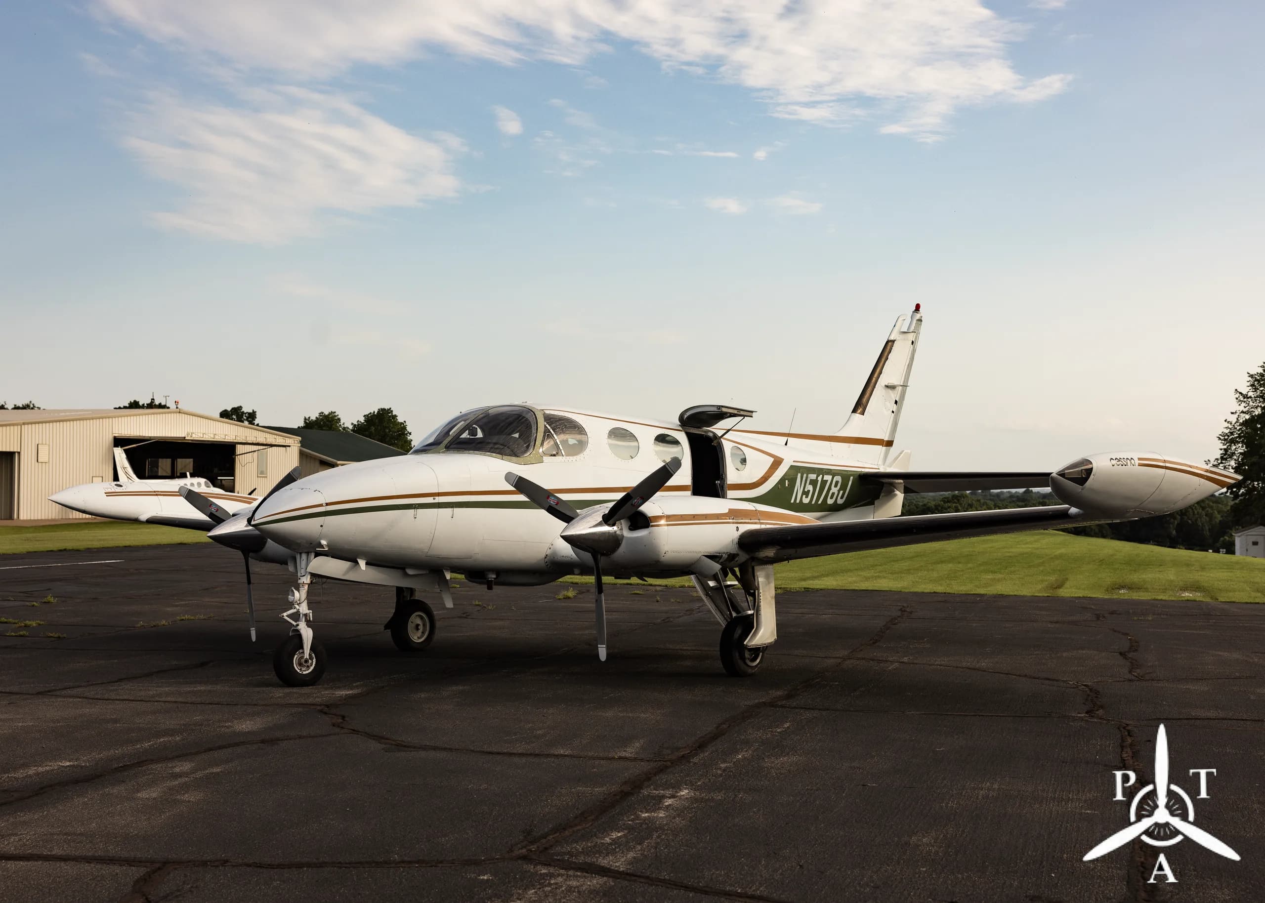 A front-side view of a white and green Cessna 340A twin-engine aircraft, N5178J, parked on an asphalt ramp.