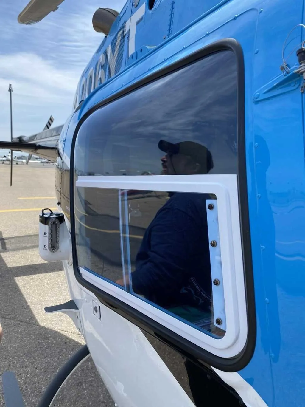 A close-up view of the cabin window of the blue Bell 206 helicopter, N206YT, with a person reflected.