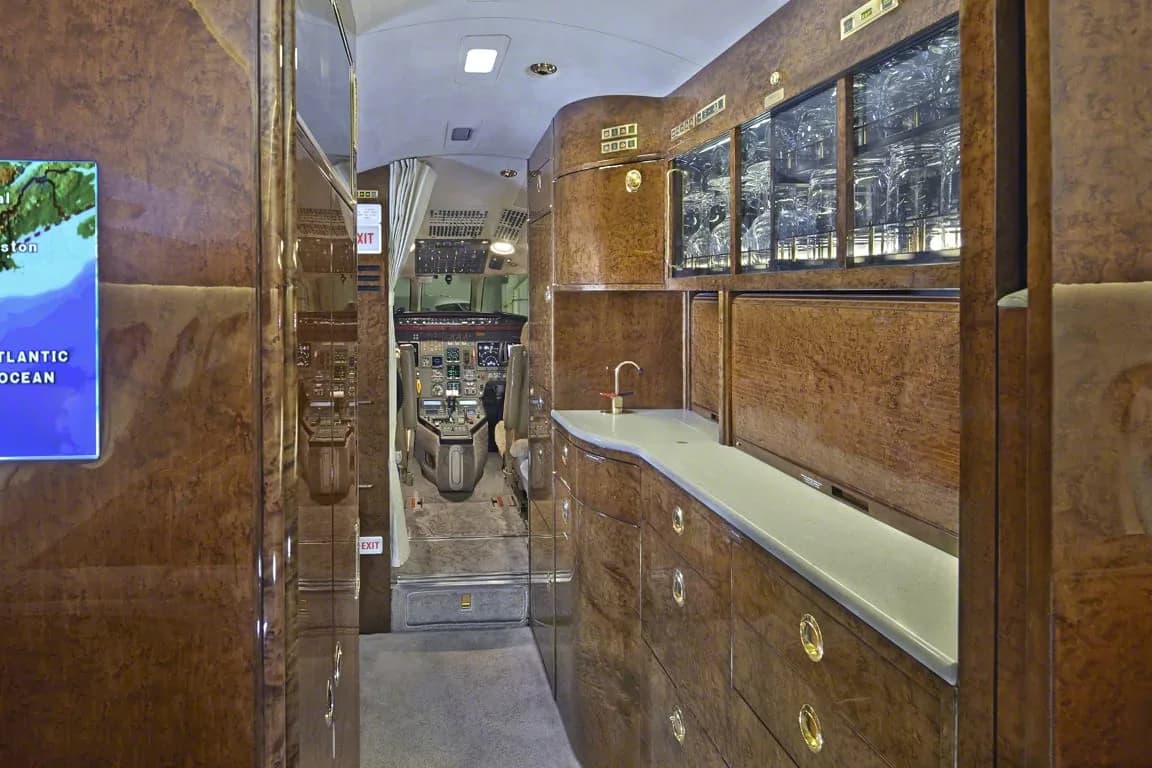 A view down the aisle of a private jet, showing the galley and a glimpse of the cockpit.