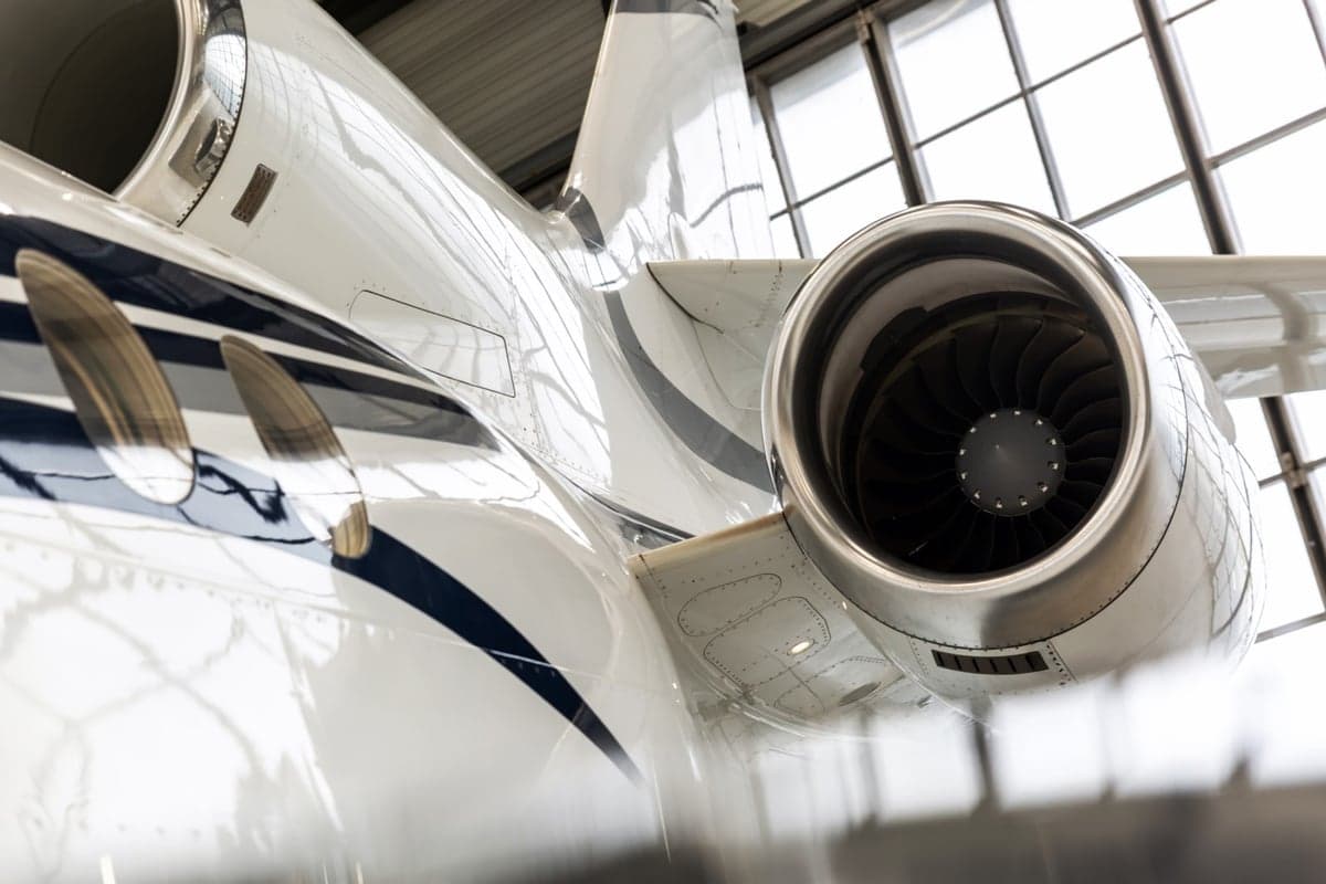 Close up of the tail and engine of a white and blue aircraft in a hangar.