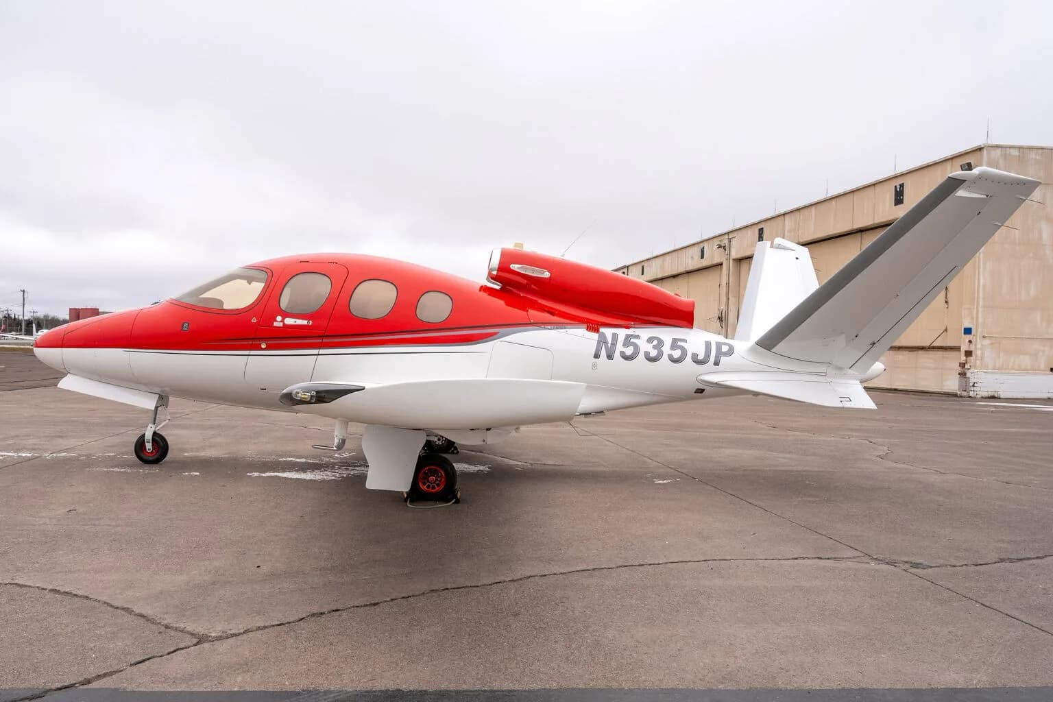 Left side view of a red and white Cirrus Vision Jet (N535JP) on the tarmac.