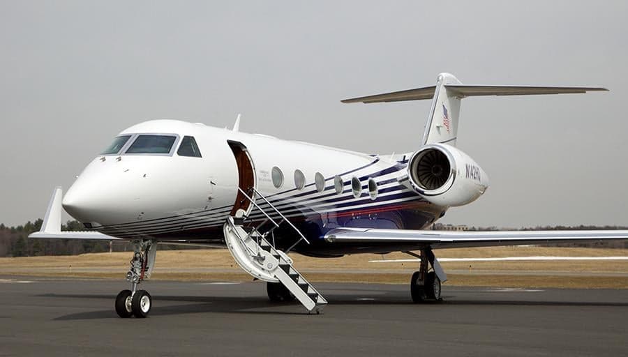 A Gulfstream G550 private jet, registration N142HQ, parked on a tarmac with its airstairs deployed, featuring a white and blue striped livery.