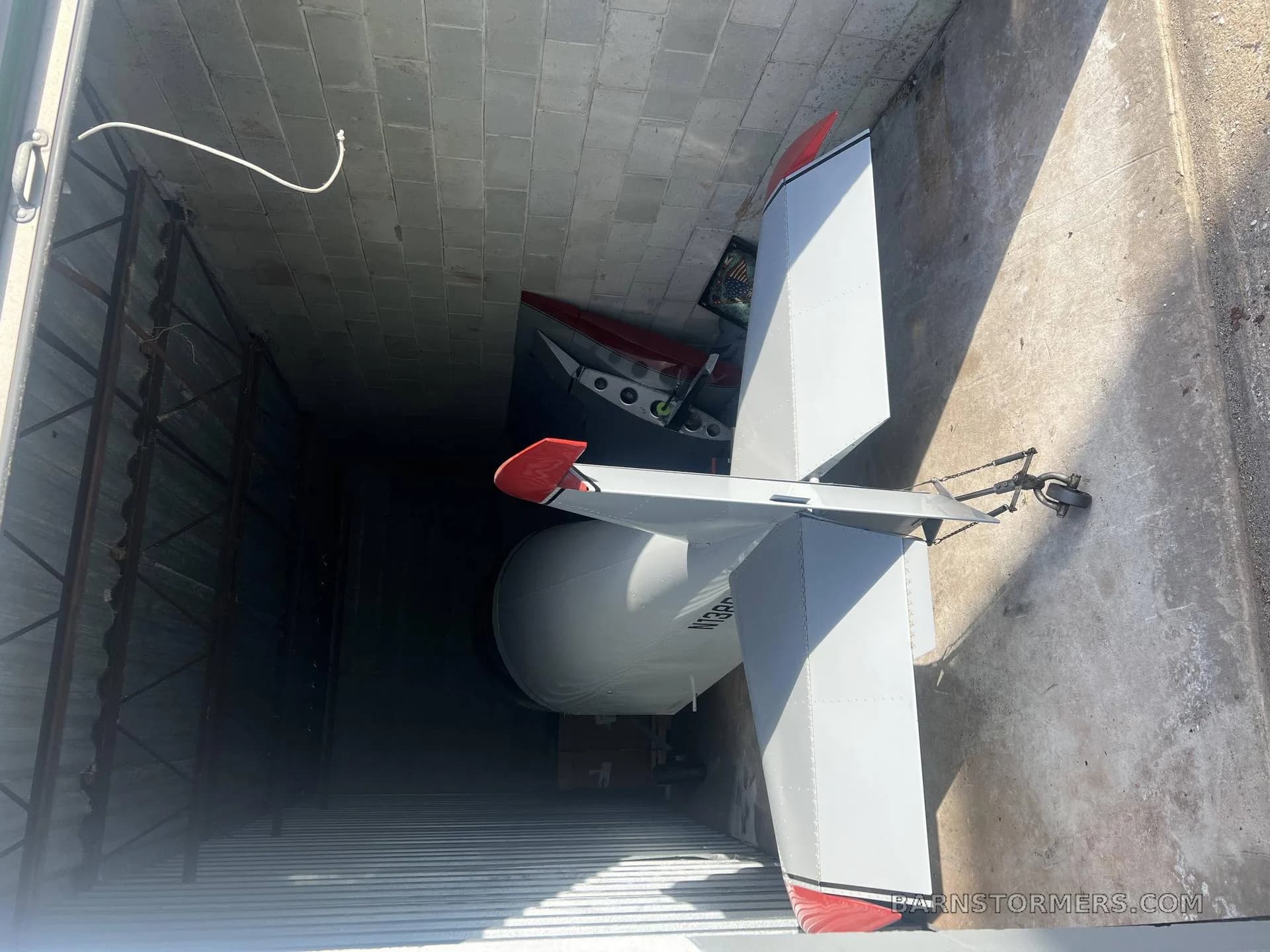 The tail section of a white aircraft with red accents, stored inside a trailer or storage unit.