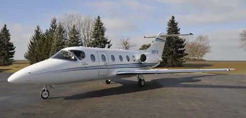 Side view of a white jet aircraft on the tarmac with trees in the background.