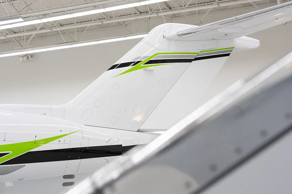 A close-up view of the white tail section of a business jet, featuring green and black stripe accents.