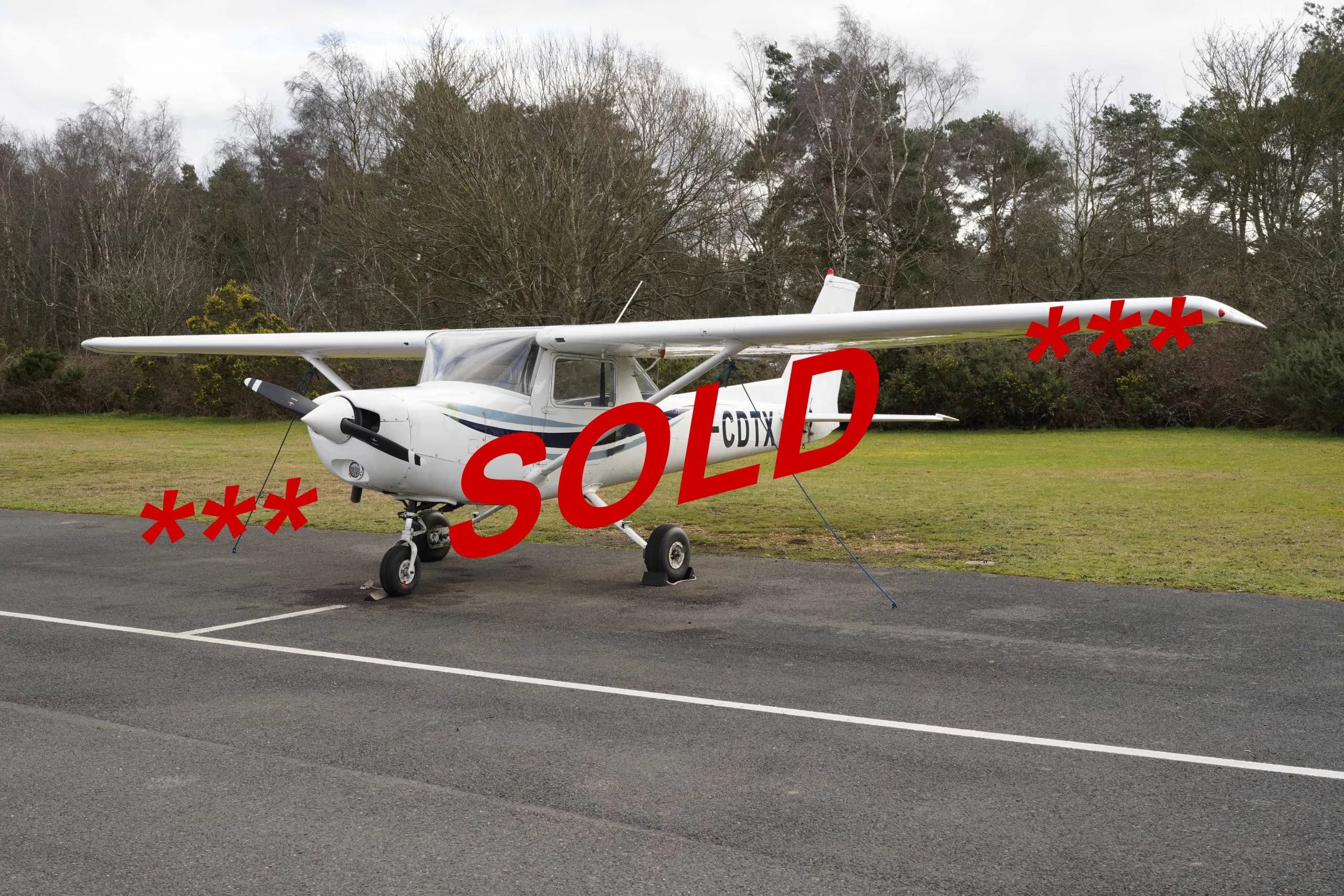 A white single-engine propeller aircraft with blue stripes, registration G-CDTX, is parked on an asphalt tarmac with trees in the background, overlaid with a red 'SOLD' text.