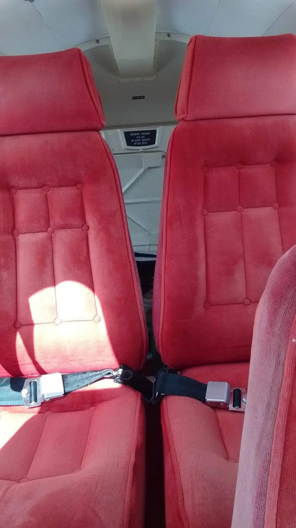 Two red fabric passenger seats with seatbelts in the interior of a small aircraft.