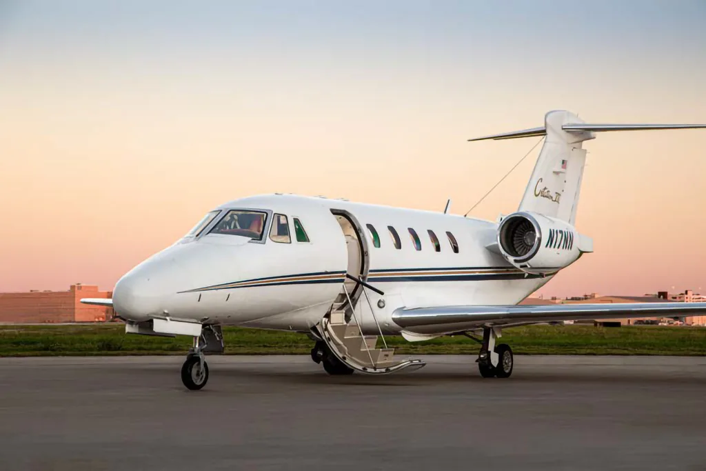A white Cessna Citation II business jet, tail number N17NN, with its door open on a tarmac at sunset.