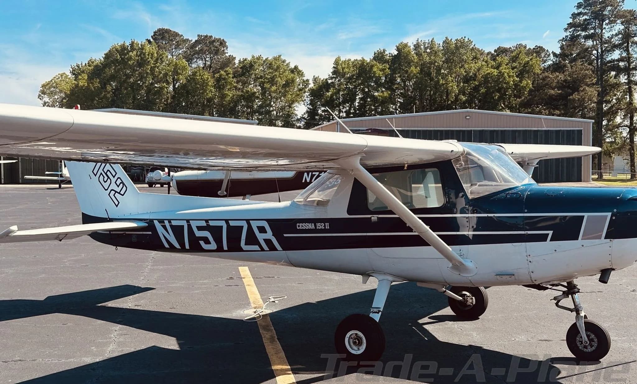 Side view of a white and blue Cessna 152 (N757ZR) with tail number visible, parked on an airfield.