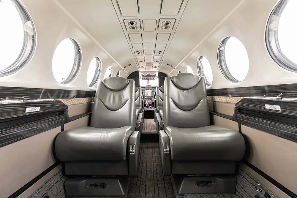 A view down the aircraft cabin aisle showing grey leather seats and large circular windows.