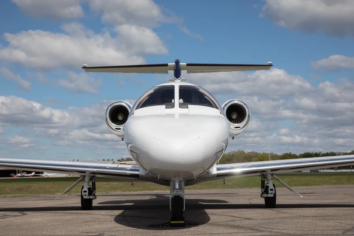 Private jet cabin with beige leather seats, extended tables, and the cockpit visible in the background.