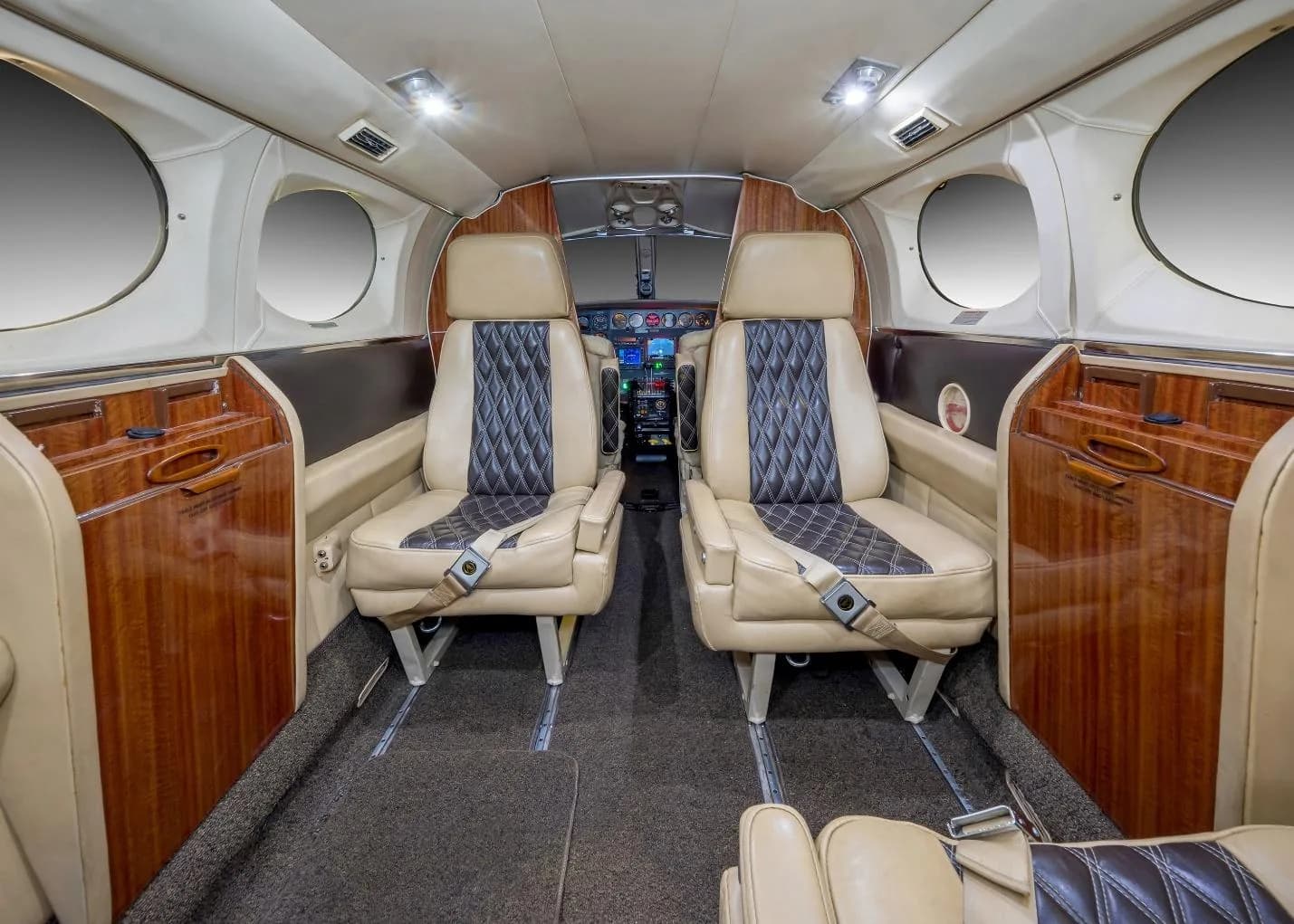 The aircraft cabin interior with beige and black quilted seats and wood paneling, looking towards the cockpit.