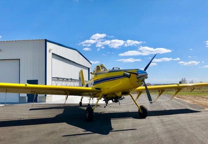 A yellow and blue Air Tractor AT-400 aircraft is parked outside a hangar on a sunny day.