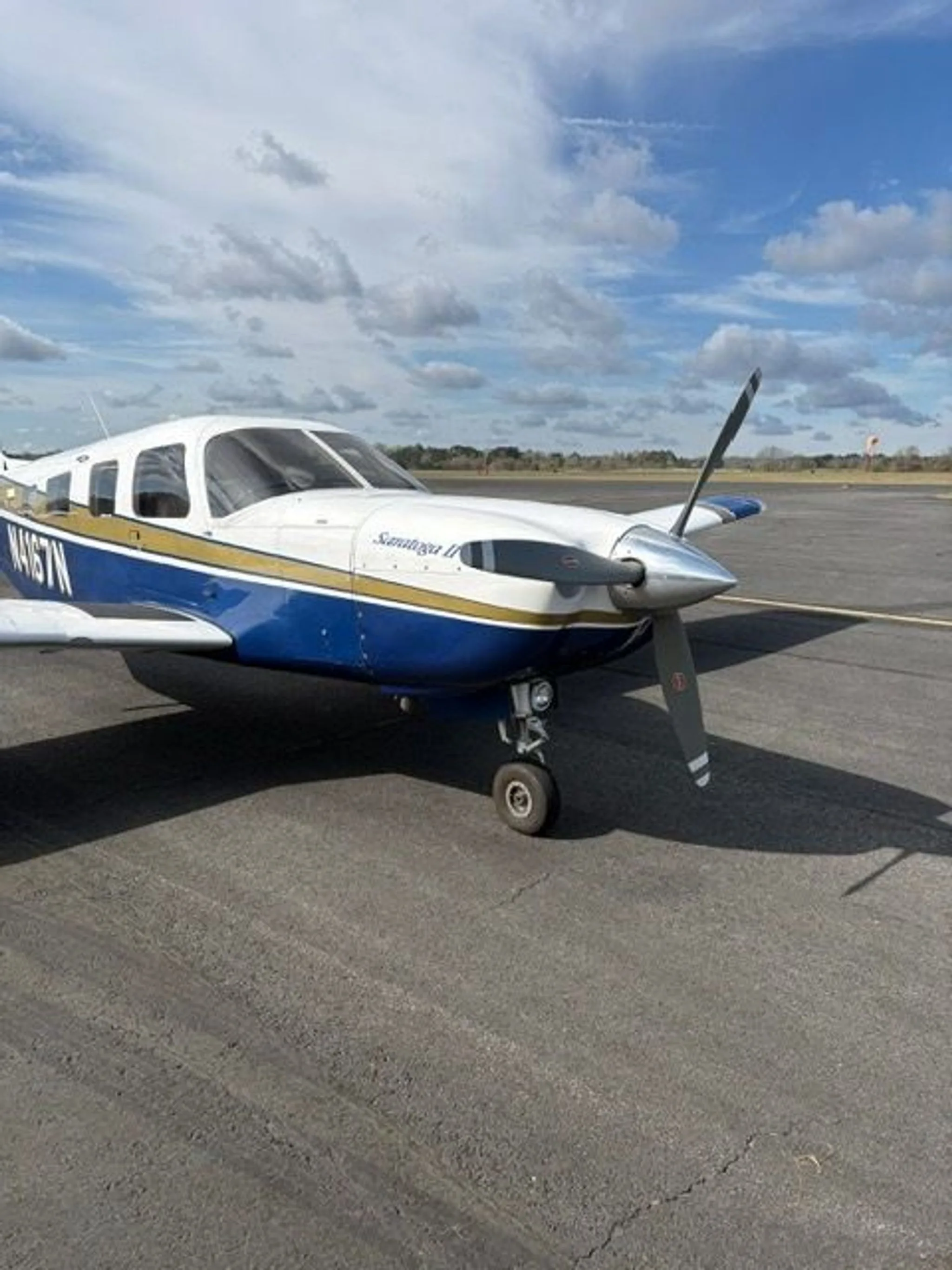 A front three-quarter view of the Piper Saratoga II TC aircraft, N4167N, with its propeller and white, blue, and gold paint.